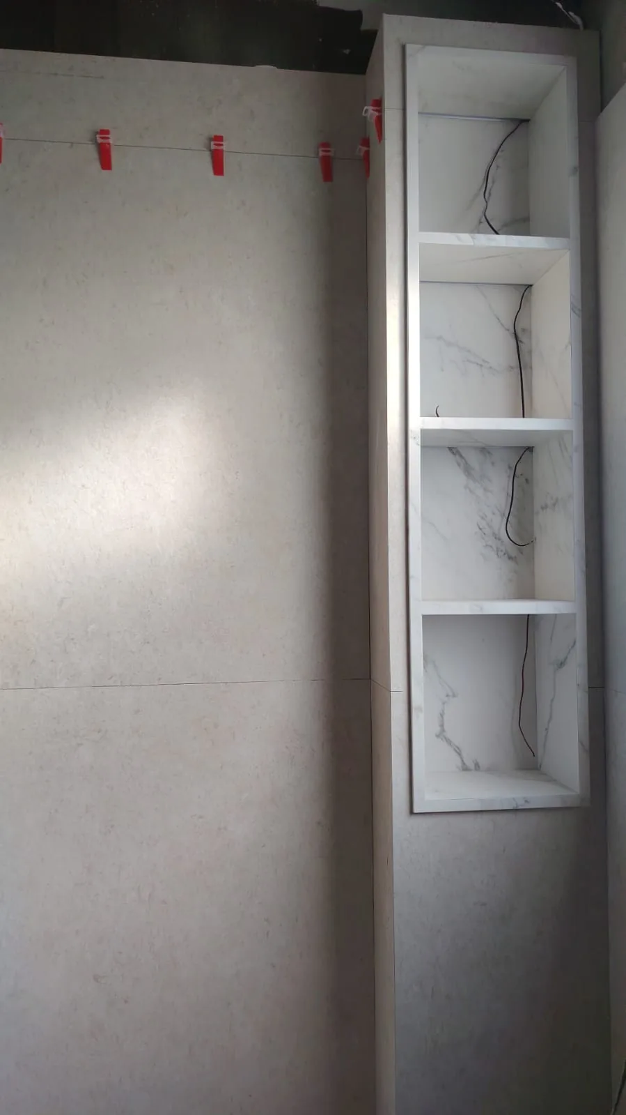 Wall tiling with levelling wedges beside a shelving niche